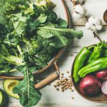 Winter vegetarian, vegan food cooking ingredients. Flat-lay of vegetables, fruit, beans, cereals, kitchen utencil, dried flowers, olive oil over white wooden background, top view. Clean eating food